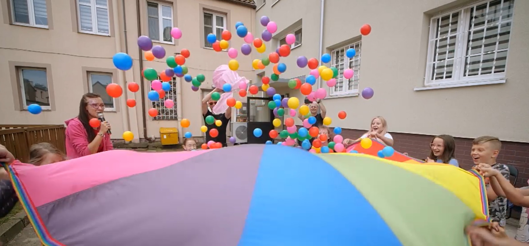 dzieci bawiące się kolorową chustą i piłeczkami 